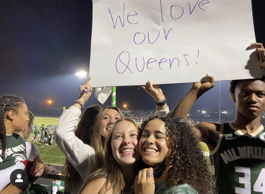 Jami Timmons and Shannon Damuth stand in front of a sign reading We love our queens during the Homecoming Football Game on October 1st. 